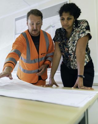 Two engineers reviewing blueprints in an office, discussing project details.
